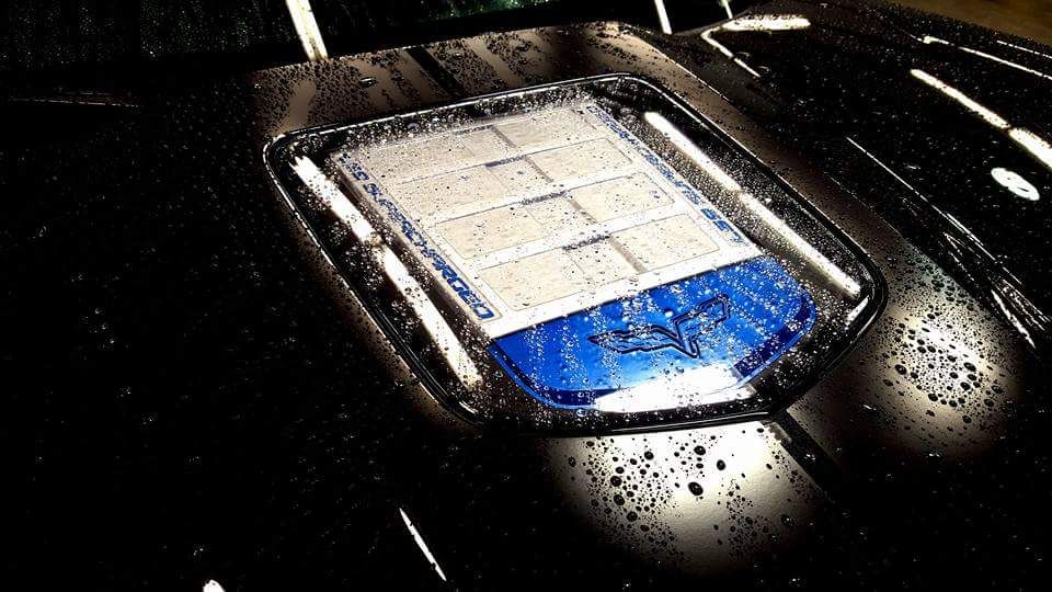 Water beads sitting on a coated black Corvette hood around the engine window